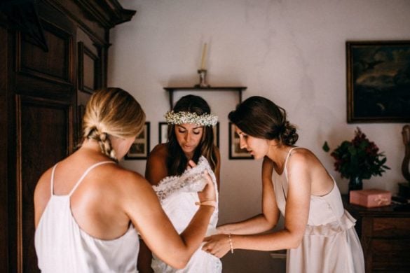 Brides maids help bride with the wedding gown